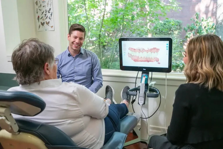 Dentist smiling while discussing dental results with a patient using a monitor display. Patients can better understand their dental treatment plans.