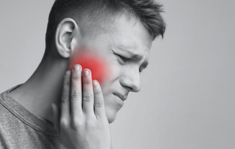Man holding his cheek with visible jaw pain caused by a possible dental problem. Hayden Dental Care provides treatment for toothaches and dental emergencies.